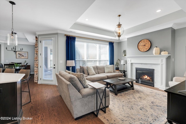 living room with dark wood-type flooring, crown molding, a tray ceiling, and an inviting chandelier