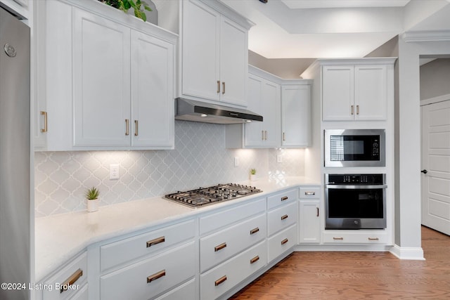 kitchen with appliances with stainless steel finishes, light hardwood / wood-style flooring, white cabinetry, and backsplash