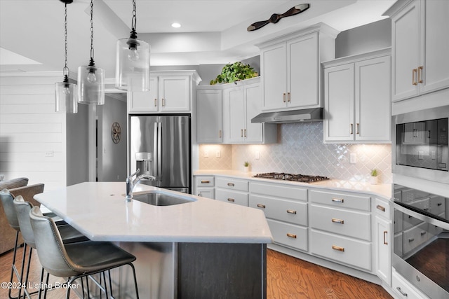 kitchen featuring appliances with stainless steel finishes, sink, light wood-type flooring, an island with sink, and pendant lighting