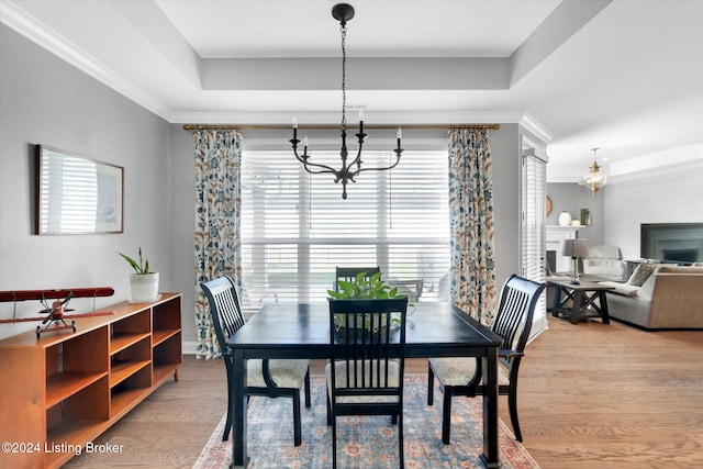 dining room with light hardwood / wood-style flooring, a notable chandelier, crown molding, and a raised ceiling