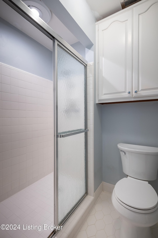 bathroom featuring tile patterned floors, a shower with door, and toilet