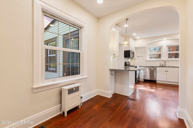 kitchen with appliances with stainless steel finishes, white cabinetry, light stone countertops, dark wood-type flooring, and pendant lighting