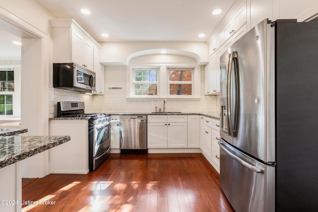 kitchen with appliances with stainless steel finishes, dark stone countertops, dark hardwood / wood-style floors, and white cabinets