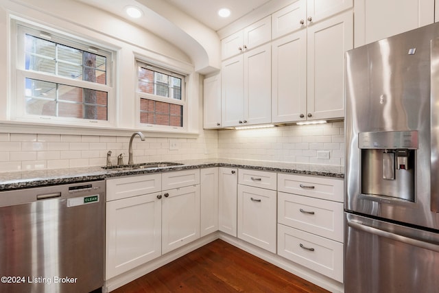 kitchen featuring appliances with stainless steel finishes, sink, white cabinetry, dark stone countertops, and dark wood-type flooring