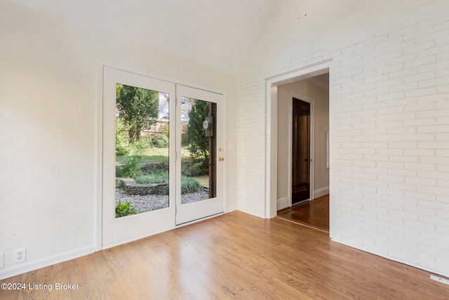 unfurnished room featuring brick wall, wood-type flooring, and lofted ceiling