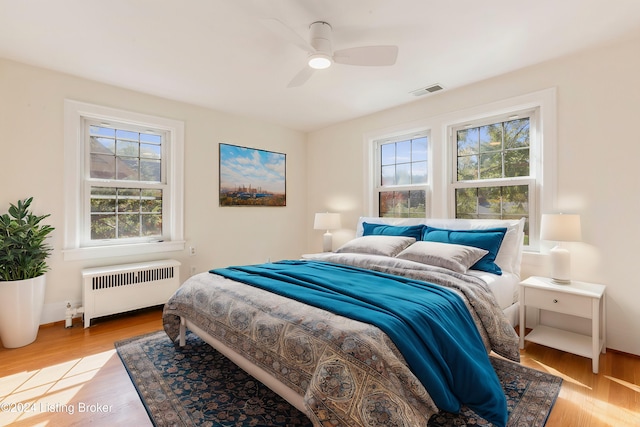 bedroom with light hardwood / wood-style floors, multiple windows, radiator, and ceiling fan