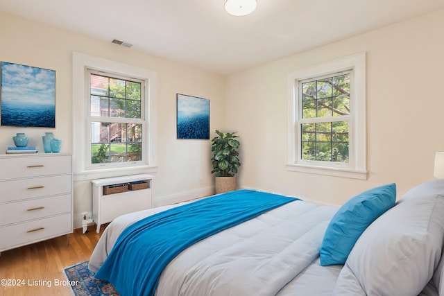 bedroom featuring light hardwood / wood-style flooring, multiple windows, and a wall unit AC