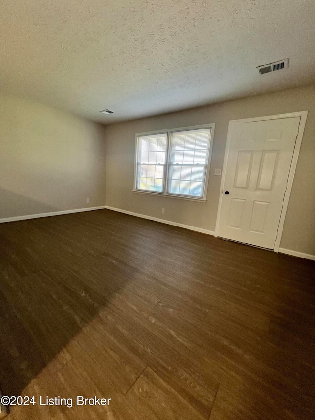 empty room with dark wood-type flooring and a textured ceiling