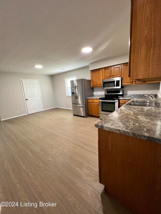 kitchen featuring sink, a textured ceiling, stainless steel appliances, dark stone counters, and light hardwood / wood-style flooring