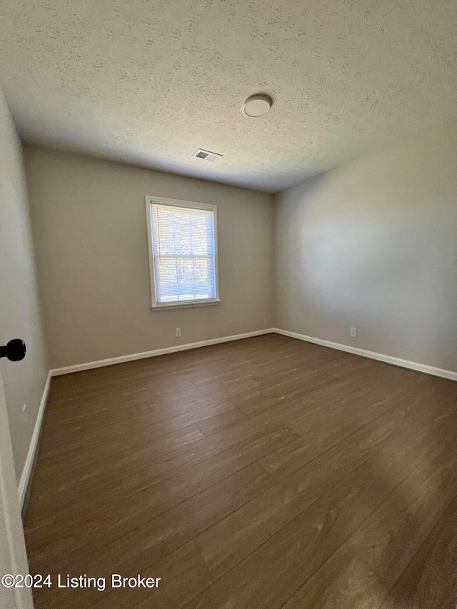 unfurnished room featuring dark wood-type flooring and a textured ceiling