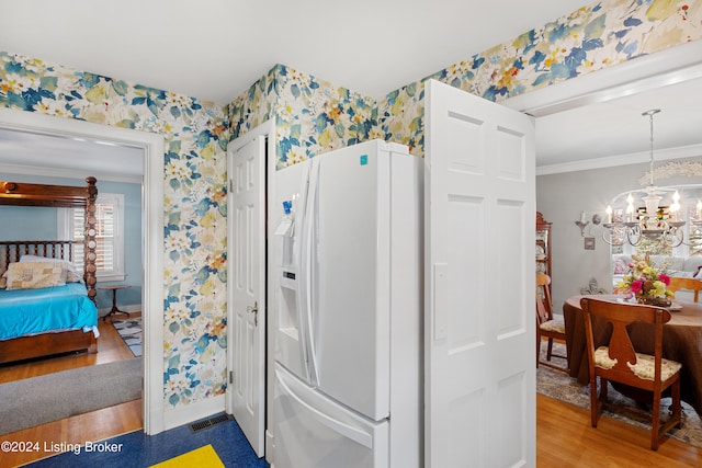 kitchen featuring hardwood / wood-style flooring, crown molding, white refrigerator with ice dispenser, pendant lighting, and a chandelier