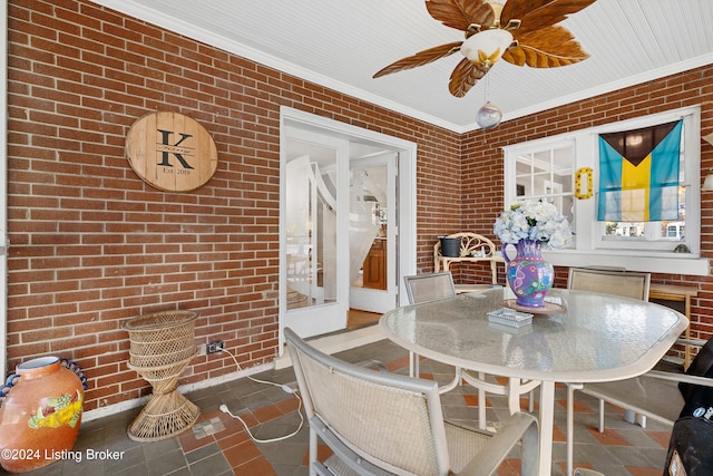 dining space with brick wall, crown molding, tile patterned flooring, and ceiling fan