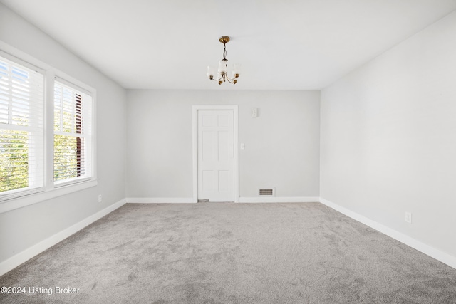 empty room with a notable chandelier and carpet flooring