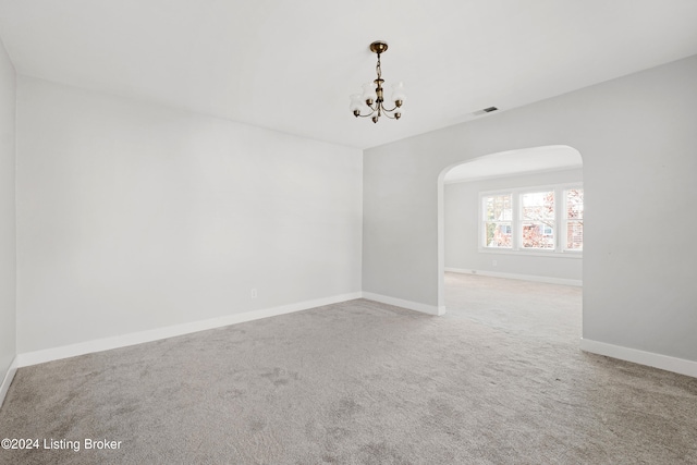 carpeted empty room featuring an inviting chandelier