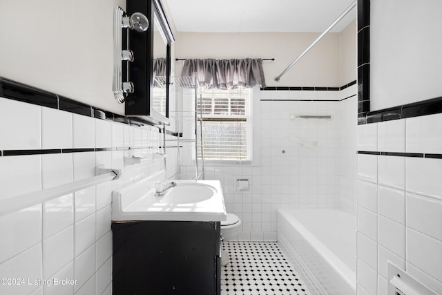 full bathroom with vanity, toilet, tiled shower / bath combo, and tile walls