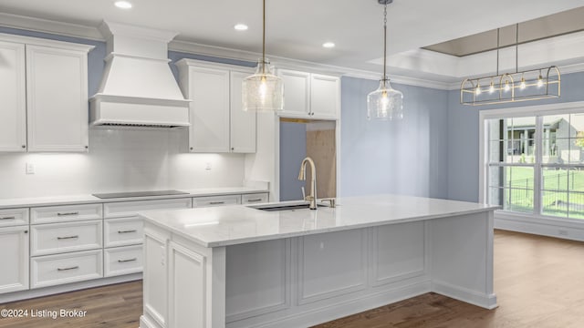 kitchen featuring sink, premium range hood, a center island with sink, white cabinets, and hardwood / wood-style flooring