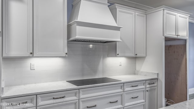 kitchen featuring decorative backsplash, light stone counters, custom exhaust hood, black electric cooktop, and white cabinetry