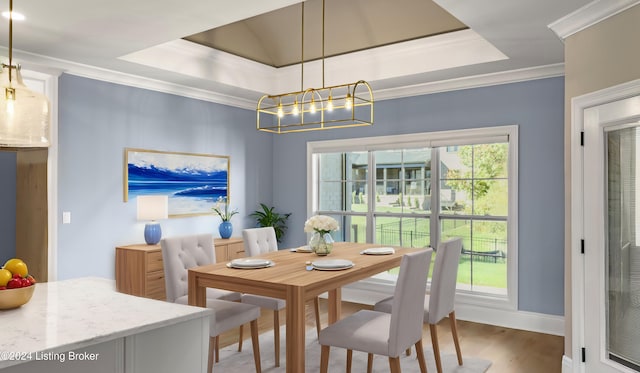 dining room featuring an inviting chandelier, hardwood / wood-style flooring, a raised ceiling, and ornamental molding