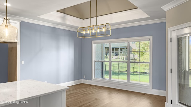 unfurnished dining area with hardwood / wood-style flooring, an inviting chandelier, a tray ceiling, and ornamental molding