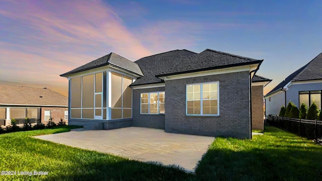 back house at dusk featuring a patio area and a yard