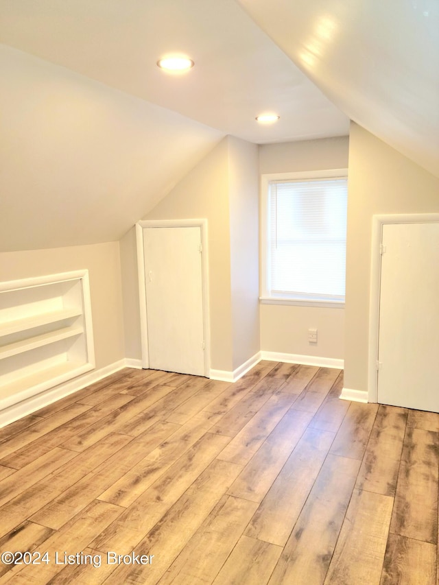 bonus room featuring lofted ceiling, built in shelves, and light wood-type flooring