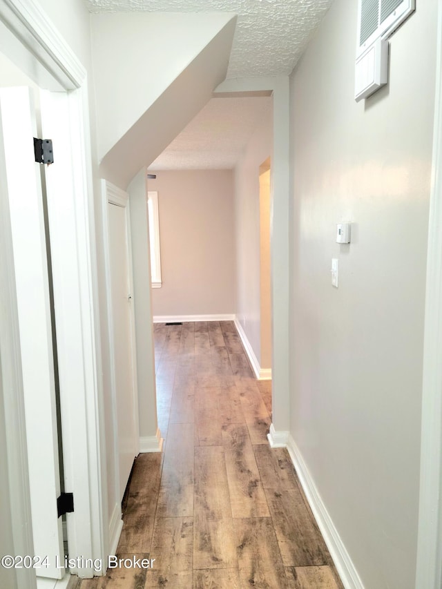 hallway with light hardwood / wood-style floors and a textured ceiling