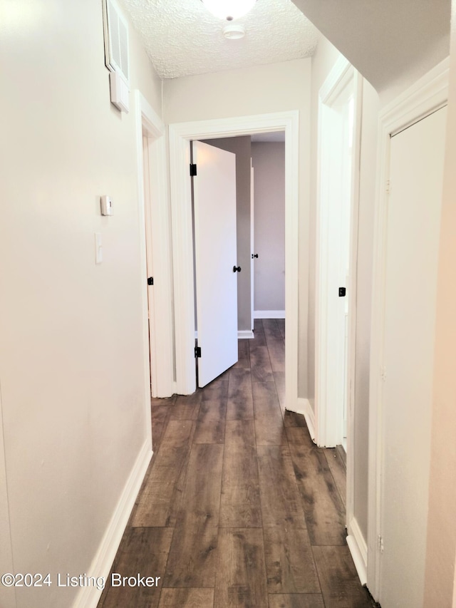 corridor with a textured ceiling and dark wood-type flooring