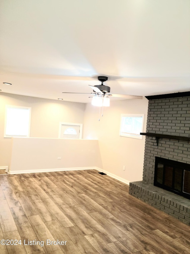 unfurnished living room featuring ceiling fan, wood-type flooring, and a brick fireplace