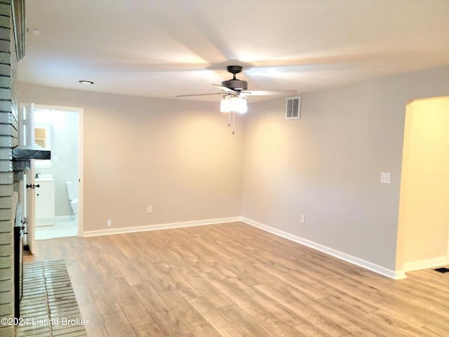 empty room featuring light hardwood / wood-style floors, a brick fireplace, and ceiling fan