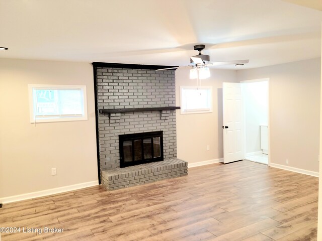 unfurnished living room featuring light hardwood / wood-style floors, a healthy amount of sunlight, ceiling fan, and a brick fireplace