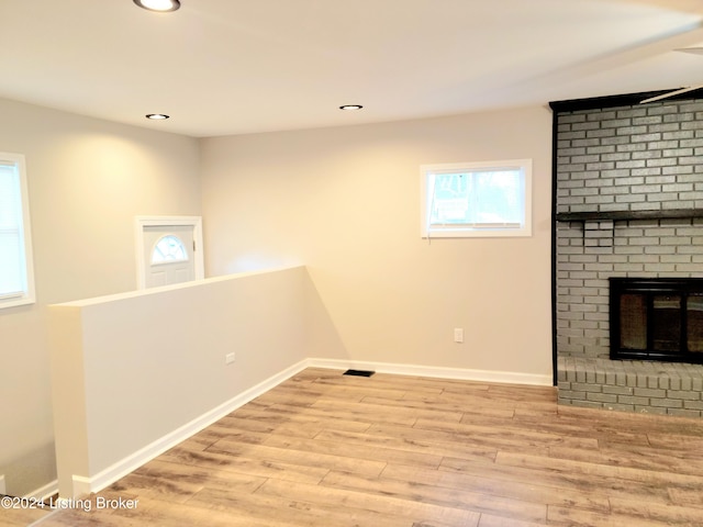 basement with light hardwood / wood-style flooring and a brick fireplace