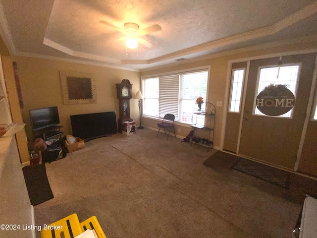 carpeted foyer featuring ornamental molding, ceiling fan, a healthy amount of sunlight, and a raised ceiling