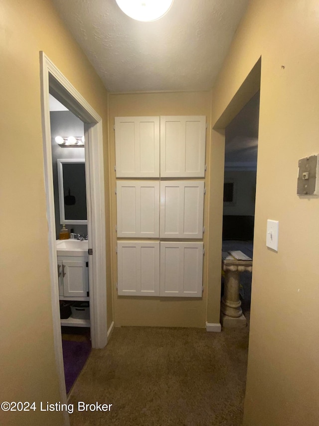 hall with sink, dark carpet, and a textured ceiling