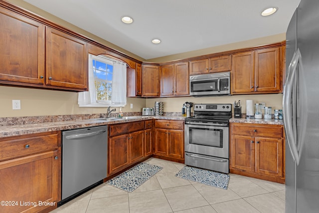 kitchen with appliances with stainless steel finishes, sink, light stone counters, and light tile patterned floors