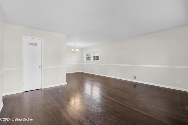 spare room with a notable chandelier and dark hardwood / wood-style flooring