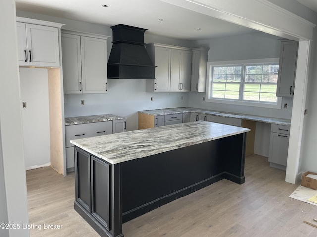 kitchen with gray cabinetry, light wood-type flooring, custom range hood, and a kitchen island