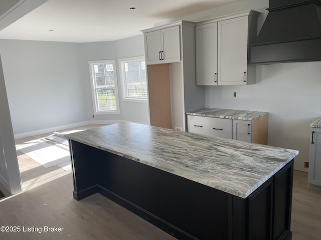 kitchen featuring gray cabinets, premium range hood, light stone countertops, a kitchen island, and light wood-type flooring