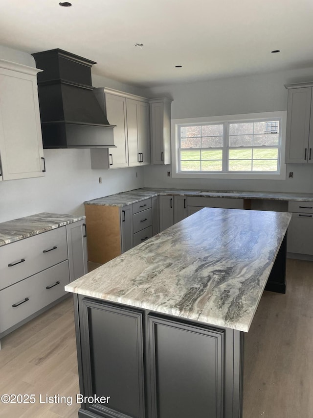 kitchen featuring light stone countertops, a center island, custom range hood, and gray cabinetry