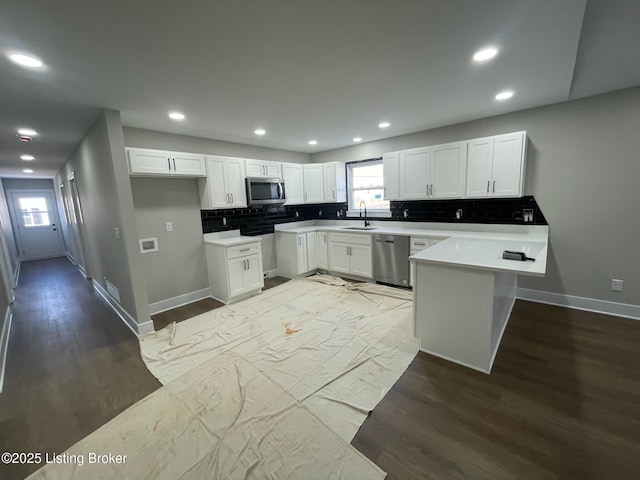 kitchen featuring dark wood-type flooring, a peninsula, stainless steel appliances, light countertops, and white cabinetry
