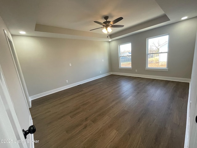 spare room featuring dark wood-style floors, a raised ceiling, ceiling fan, and baseboards