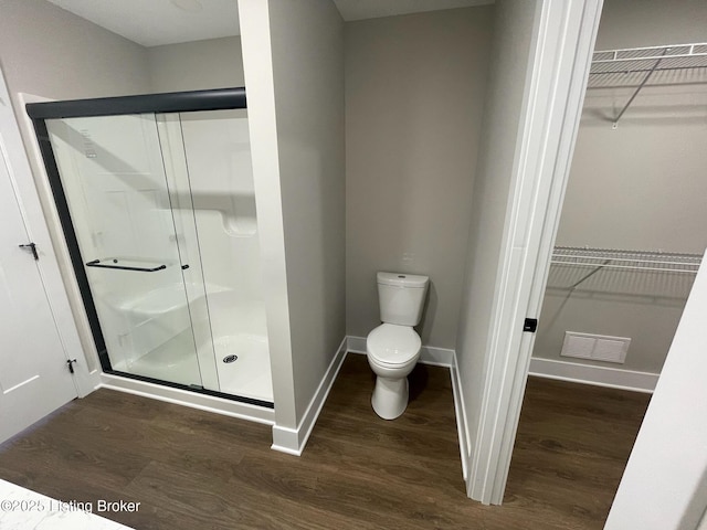 full bath featuring a stall shower, a walk in closet, and wood finished floors