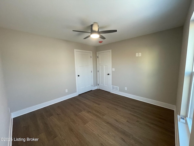 empty room featuring dark wood-type flooring, visible vents, ceiling fan, and baseboards
