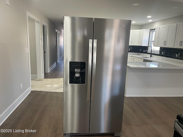 kitchen featuring a sink, white cabinetry, light countertops, stainless steel fridge, and dark wood finished floors