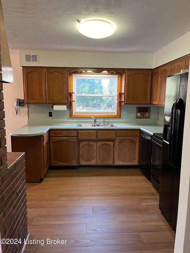 kitchen with a textured ceiling, light hardwood / wood-style floors, black appliances, and sink