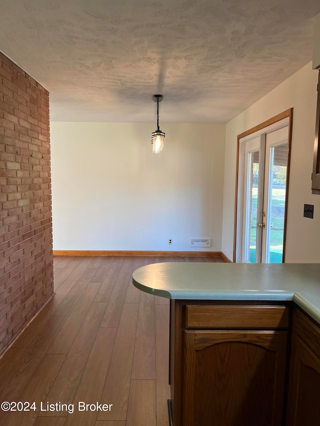 kitchen featuring a textured ceiling, brick wall, decorative light fixtures, and light wood-type flooring