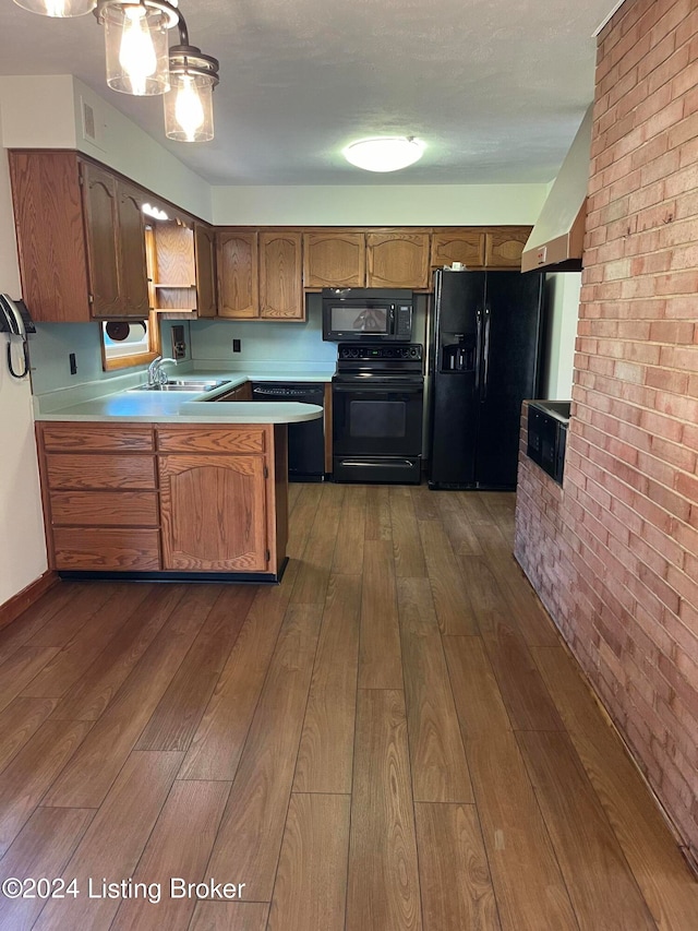 kitchen with sink, brick wall, dark hardwood / wood-style floors, kitchen peninsula, and black appliances