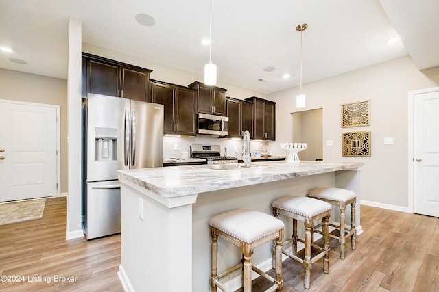 kitchen featuring stainless steel appliances, hanging light fixtures, a center island with sink, and light wood-type flooring