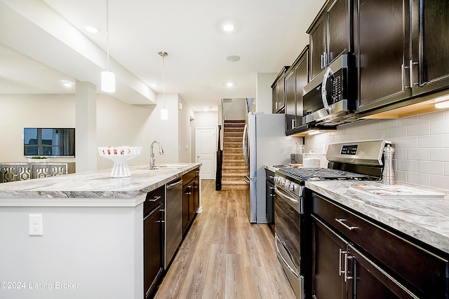 kitchen featuring light hardwood / wood-style floors, sink, appliances with stainless steel finishes, hanging light fixtures, and a kitchen island with sink