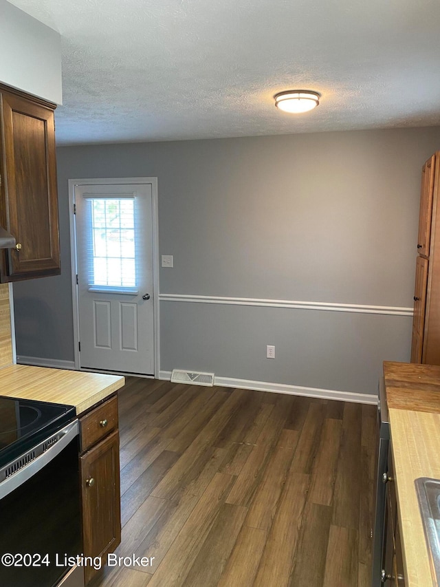kitchen with butcher block counters, electric range oven, a textured ceiling, and dark hardwood / wood-style floors