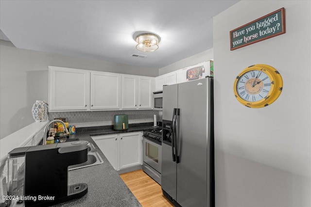 kitchen featuring white cabinetry, decorative backsplash, appliances with stainless steel finishes, and light hardwood / wood-style flooring